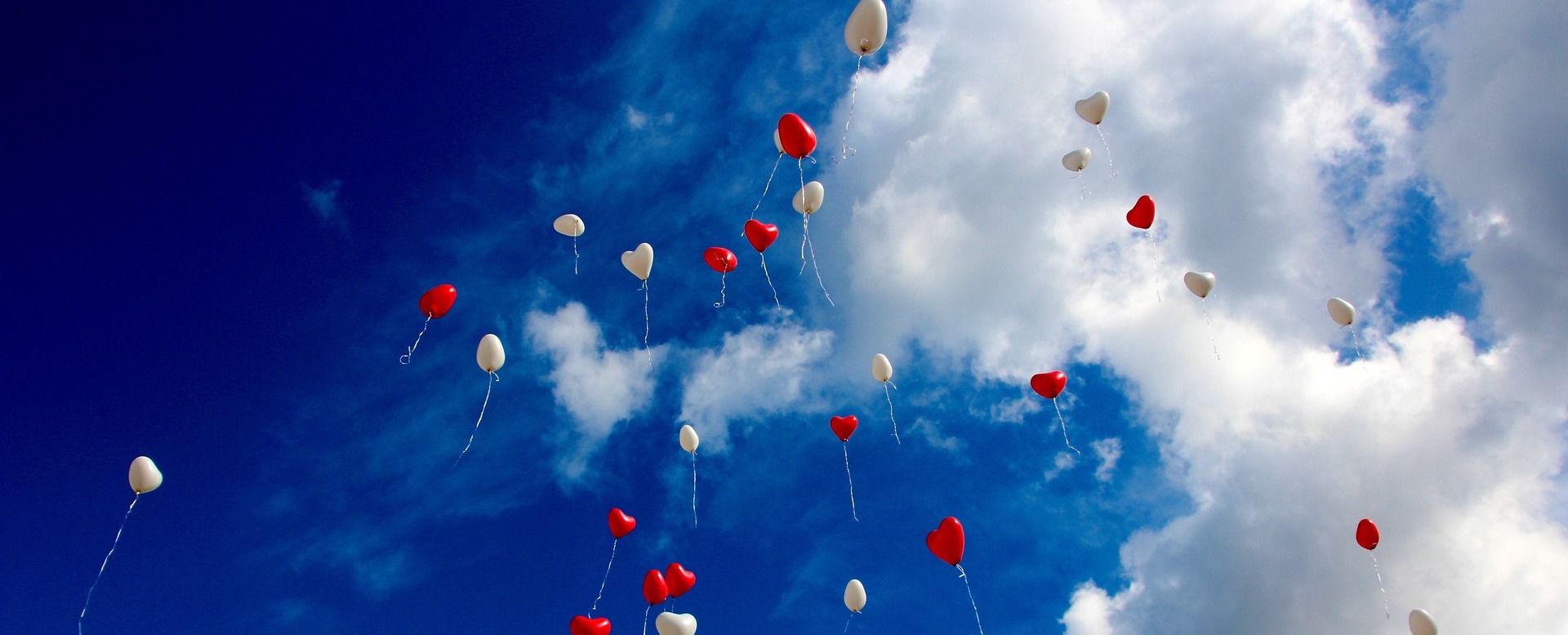 Herzballons in rot und weiß vor blauem Himmel.